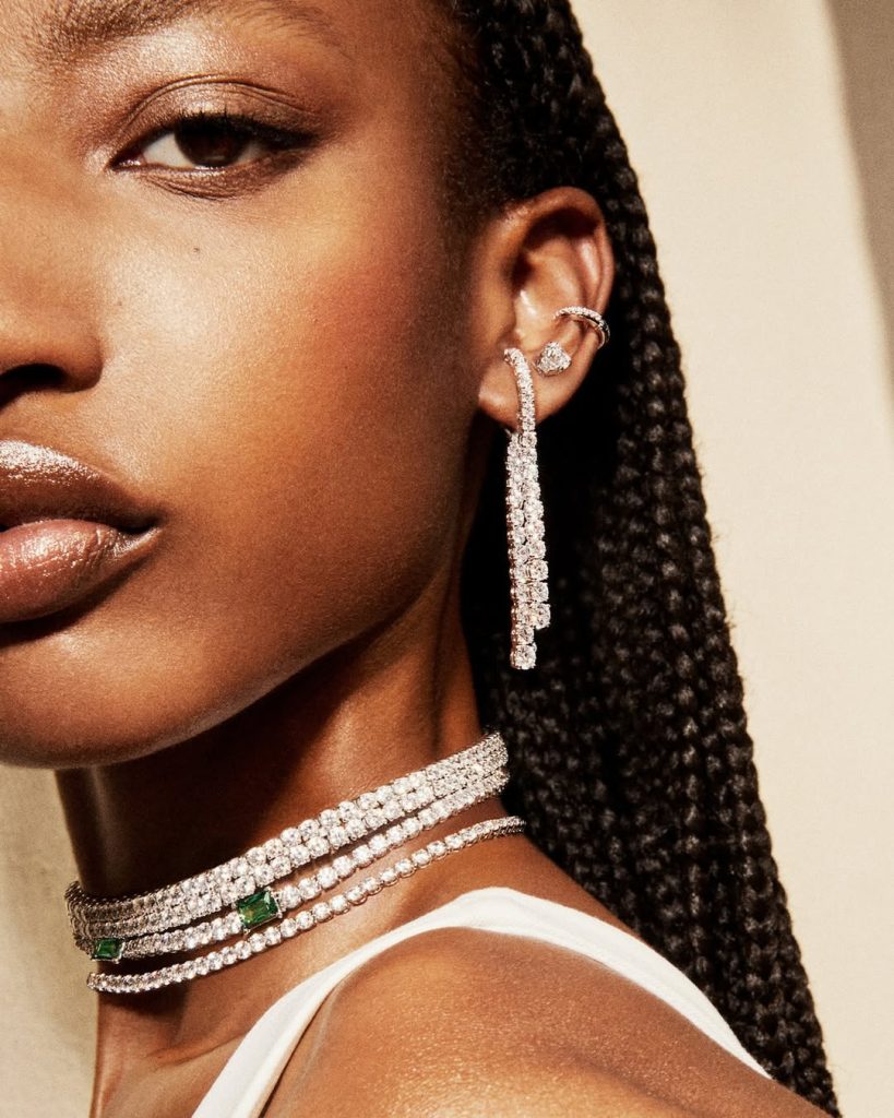 Mulher usando colar e brincos Swarovski cravejados de cristais, com design elegante e sofisticado, em destaque contra fundo neutro.